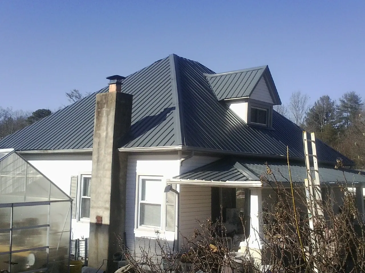 Dark blue standing seam metal roof on a white farmhouse with dormer — Slate & Tile Roof Repair by Roofing Brothers in Dexter City