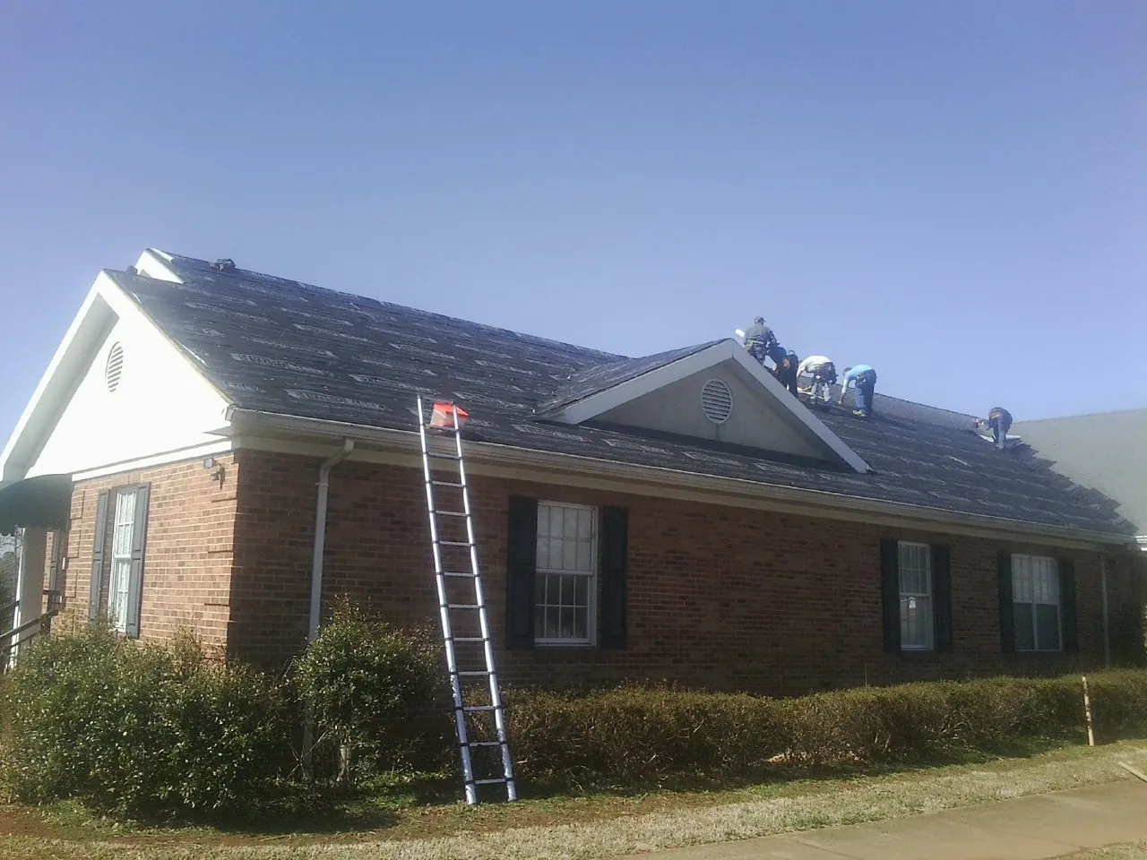 Crew tearing shingles off a brick ranch roof with a ladder set — Emergency Roof Repair work by our crew in Dexter City
