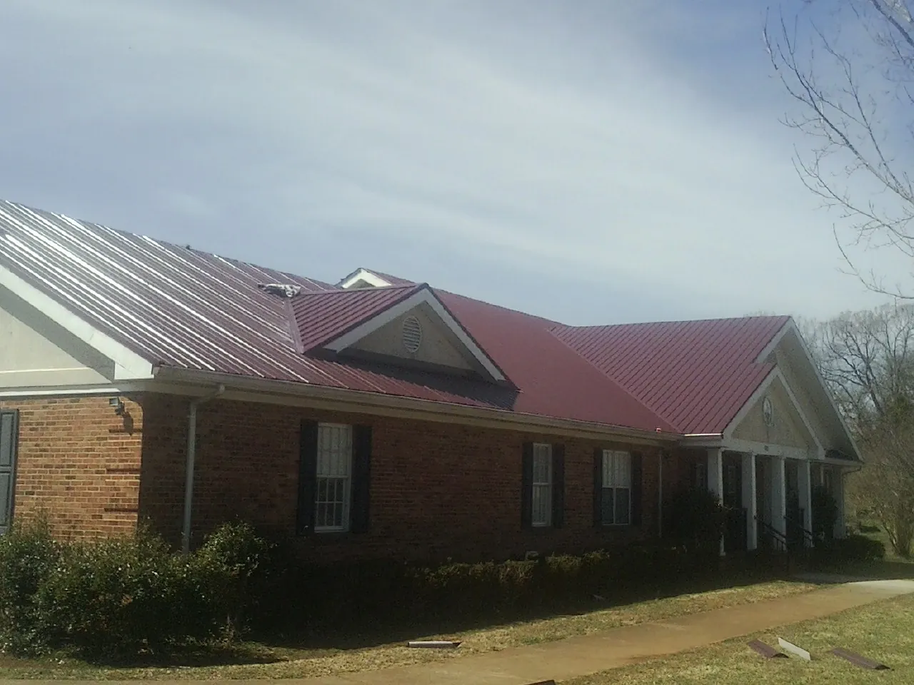 Red metal roof with gabled entries on a long brick building, from a Hail Damage Roof Repair job in Dexter City
