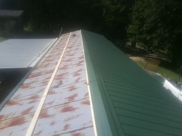 Old rusted panels beside newly installed green metal roofing — Wind Damage Roof Repair by Roofing Brothers in Dexter City