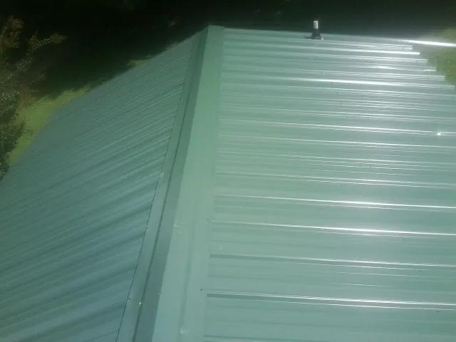 New green metal panels meeting at the ridge of a roof — Flat Roof Repair work by our crew in Dexter City