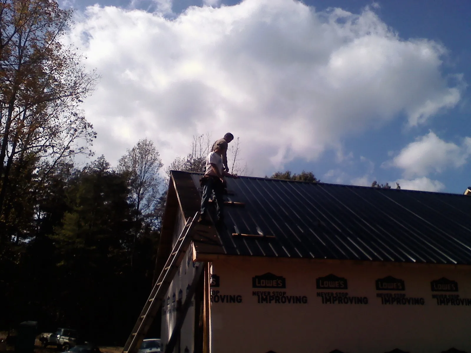 Roofer fastening dark metal panels high against a cloudy sky, from a Roof Inspection job in Dexter City