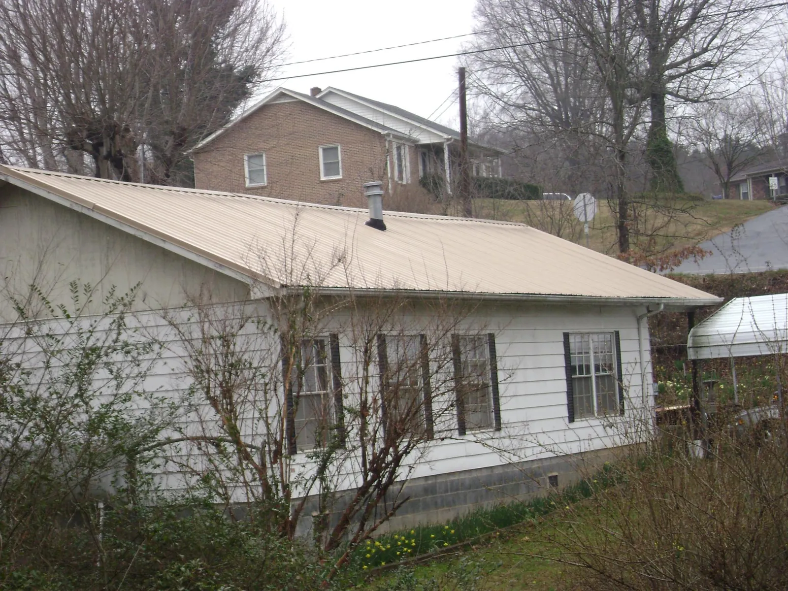 Tan metal roof on a white sided house set into a hillside — Commercial Roofing by Roofing Brothers in Dexter City