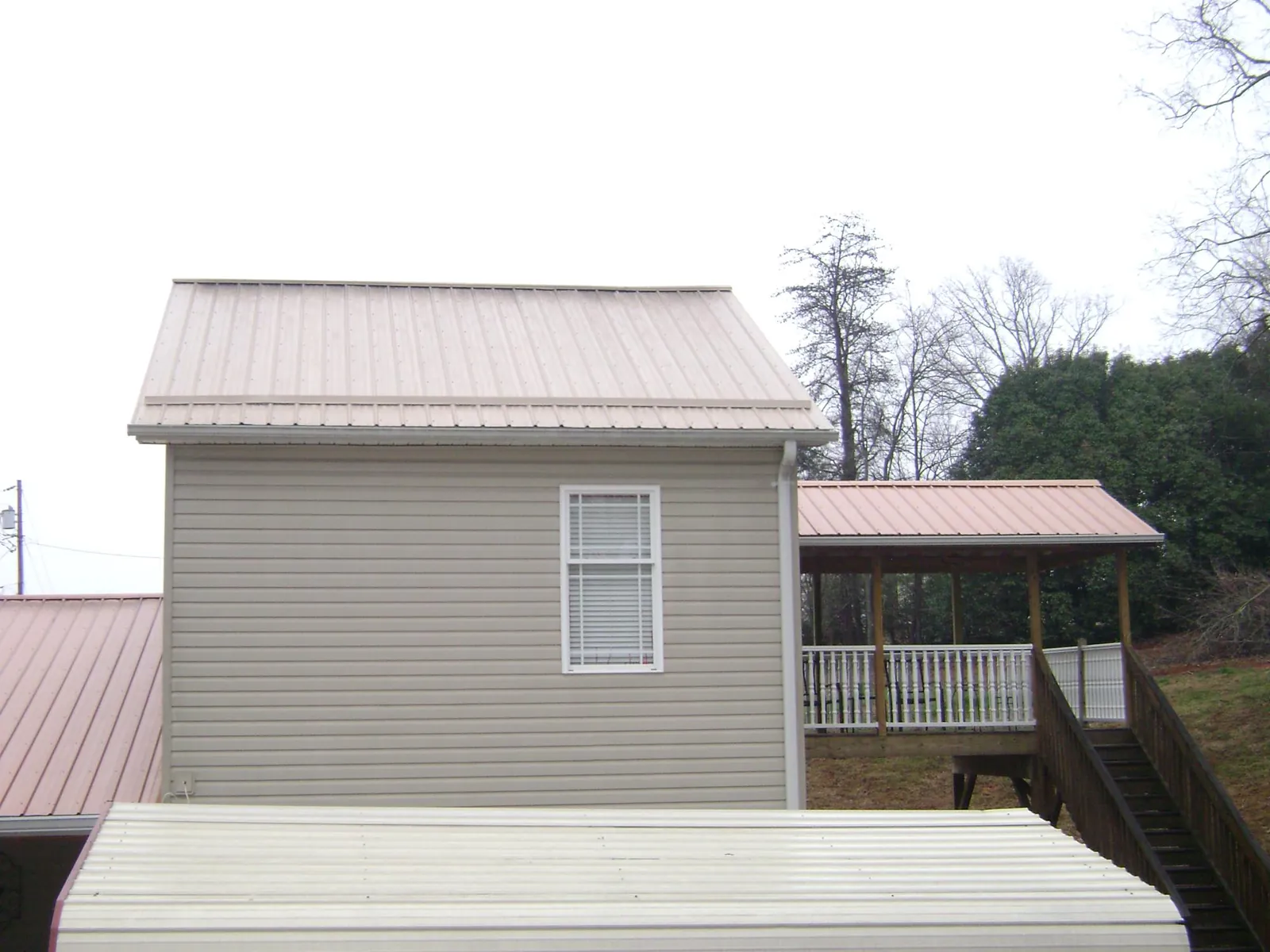 Tan metal roofs on a two story addition and attached porch, from a Roof Replacement job in Dexter City